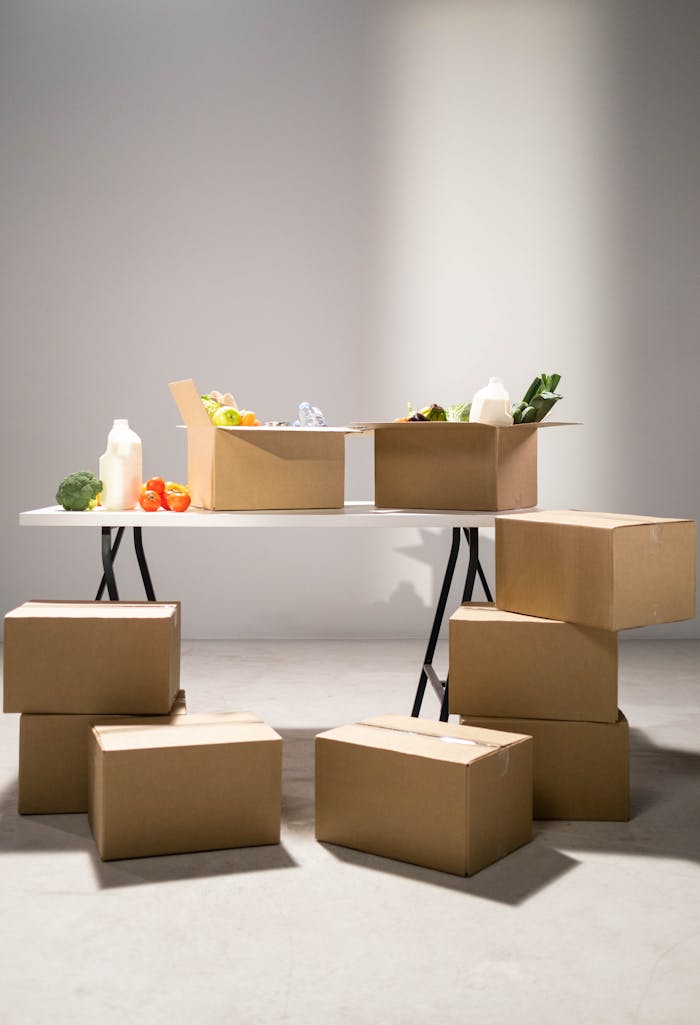 home-hero-bg Cardboard boxes filled with assorted groceries on a white folding table indoors.